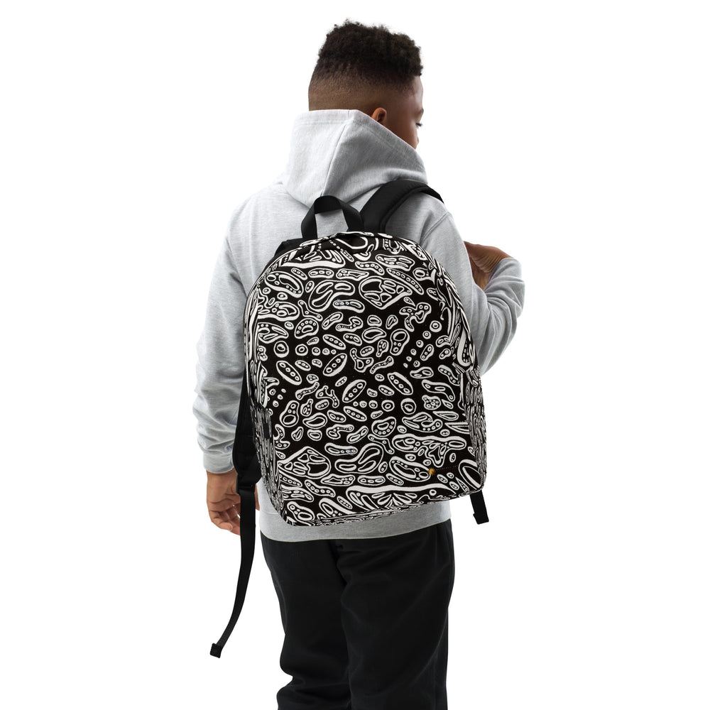 Lifestyle shot, right-front angle on model wearing the Penumbra backpack. The backpack displays a bold all-over abstract design; padded shoulder straps for comfortable everyday commuting and travel in the USA. Nicholas Hayes Art.