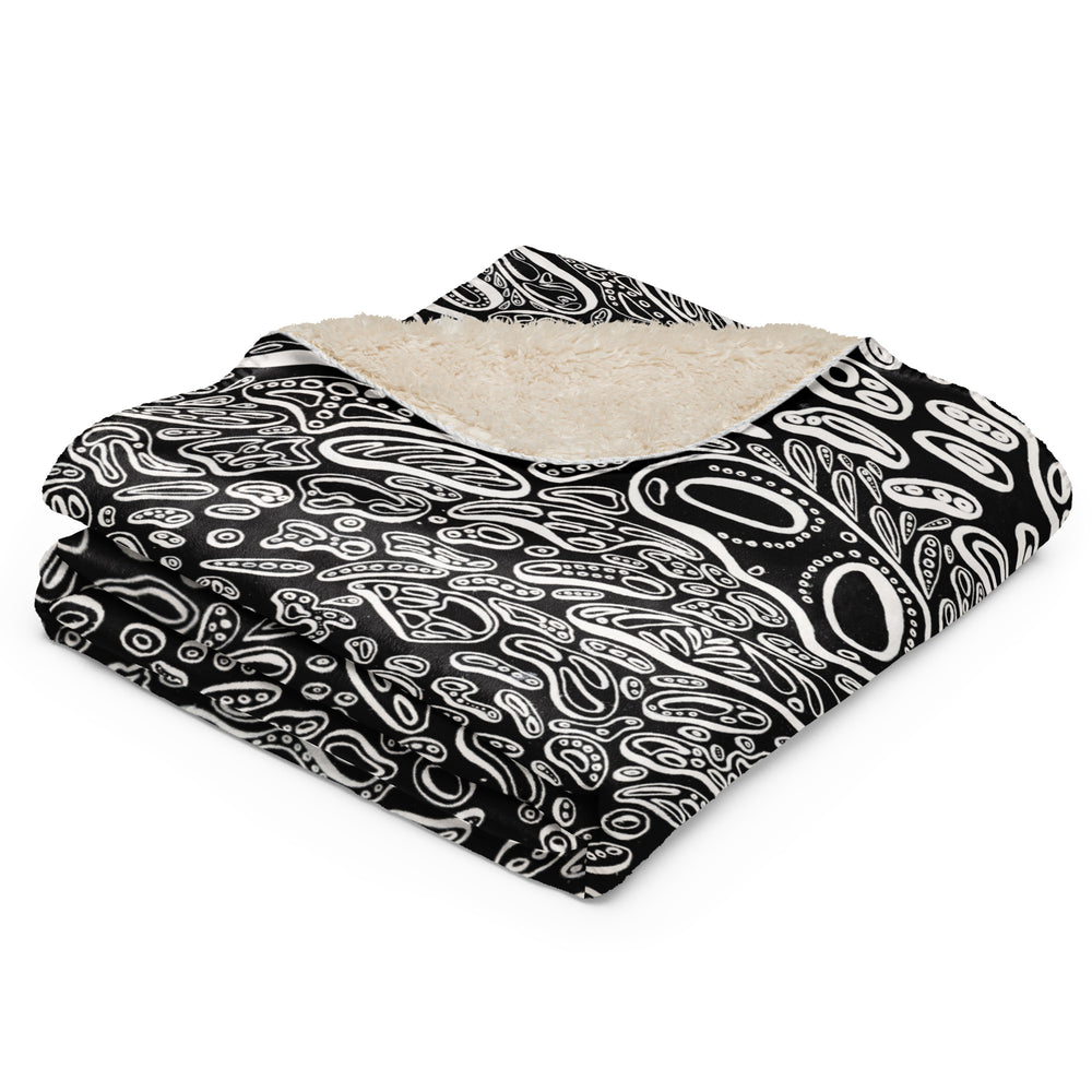 Folded Penumbra Painting No. 1 sherpa blanket with corner flipped to reveal fluffy sherpa fleece and smooth printed surface; highlights cozy texture, premium feel, and gift-ready presentation. Black backdrop with white cellular shapes. Psychedelic art by Nicholas Hayes, a Chicago based visual artist.