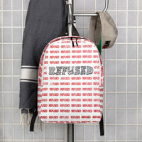 Lifestyle hanger shot of the Refused backpack—white shell with all-over red “REFUSED” print and bold black wordmark displayed against tiled wall to show modern aesthetic and scale. design by optical artist Nicholas Hayes, Chicago Illinois. 