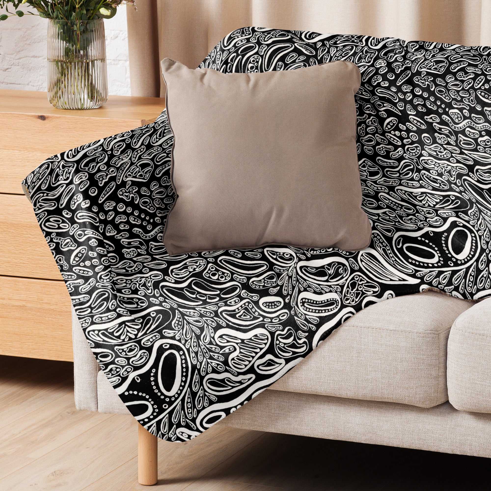 A black and white sherpa blanket draped over a chair in a neutral room. Bold abstract artwork used as a modern décor accent while showcasing its soft, winter-ready warmth. Art by Nicholas Hayes a trippy psychedelic artist from Chicago.