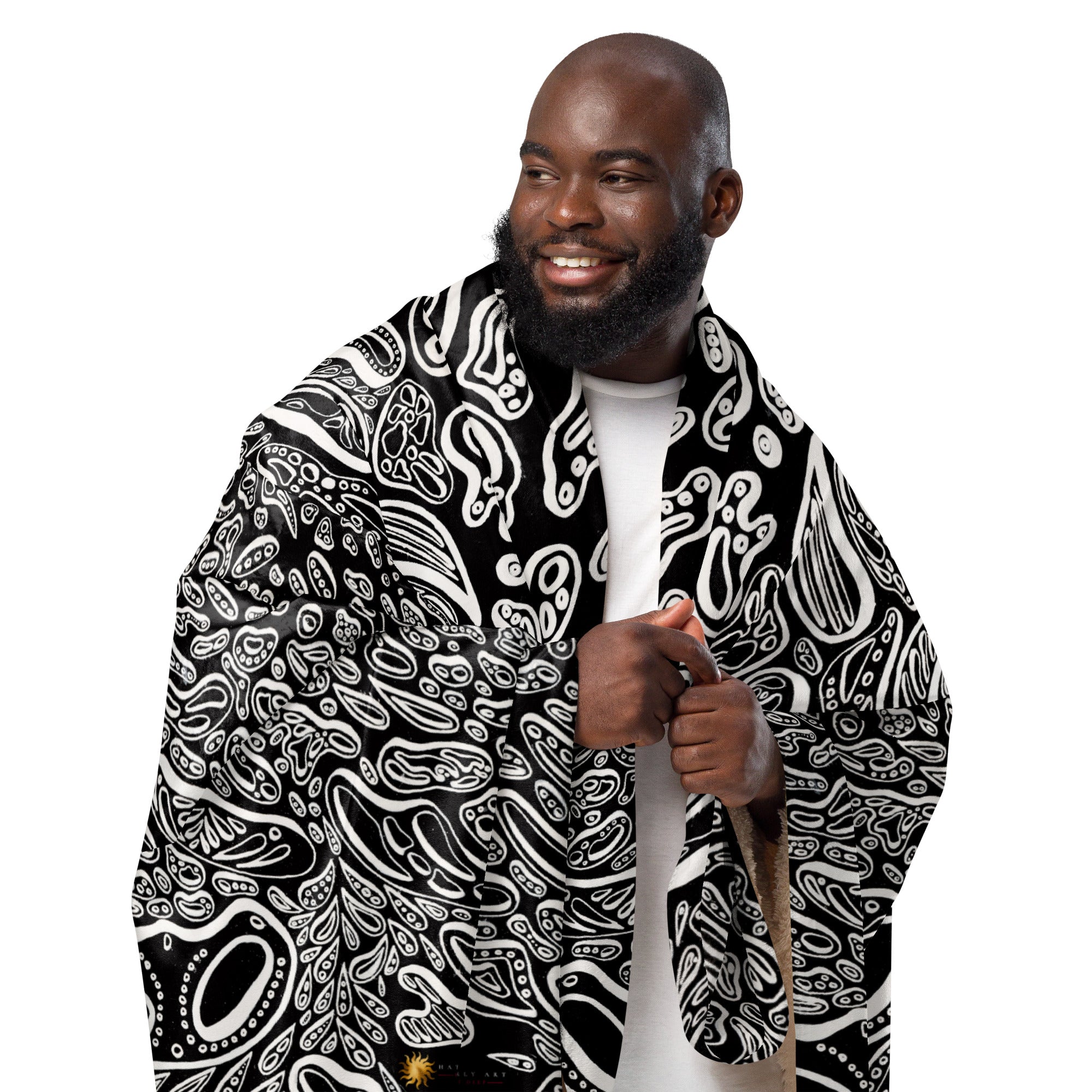 Lifestyle scale image of a black make with the Penumbra No. 1 sherpa blanket wrapped around him and held up vertically. The blanket is a full abstract design with a black backdrop and white shapes floating creating a three dimensional look. Lightweight, warm polyester sherpa ideal for living rooms, bedrooms, or studios. Art by Nicholas Hayes.