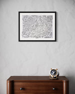 A framed abstract artwork by Chicago based emerging artist Nicholas Hayes hanging on a wall above a wooden furniture piece, with a wall clock on the furniture. Original 18×24 acrylic on heavyweight canvas paper, professionally framed and ready to hang; one-of-a-kind contemporary artwork for modern home or gallery walls.