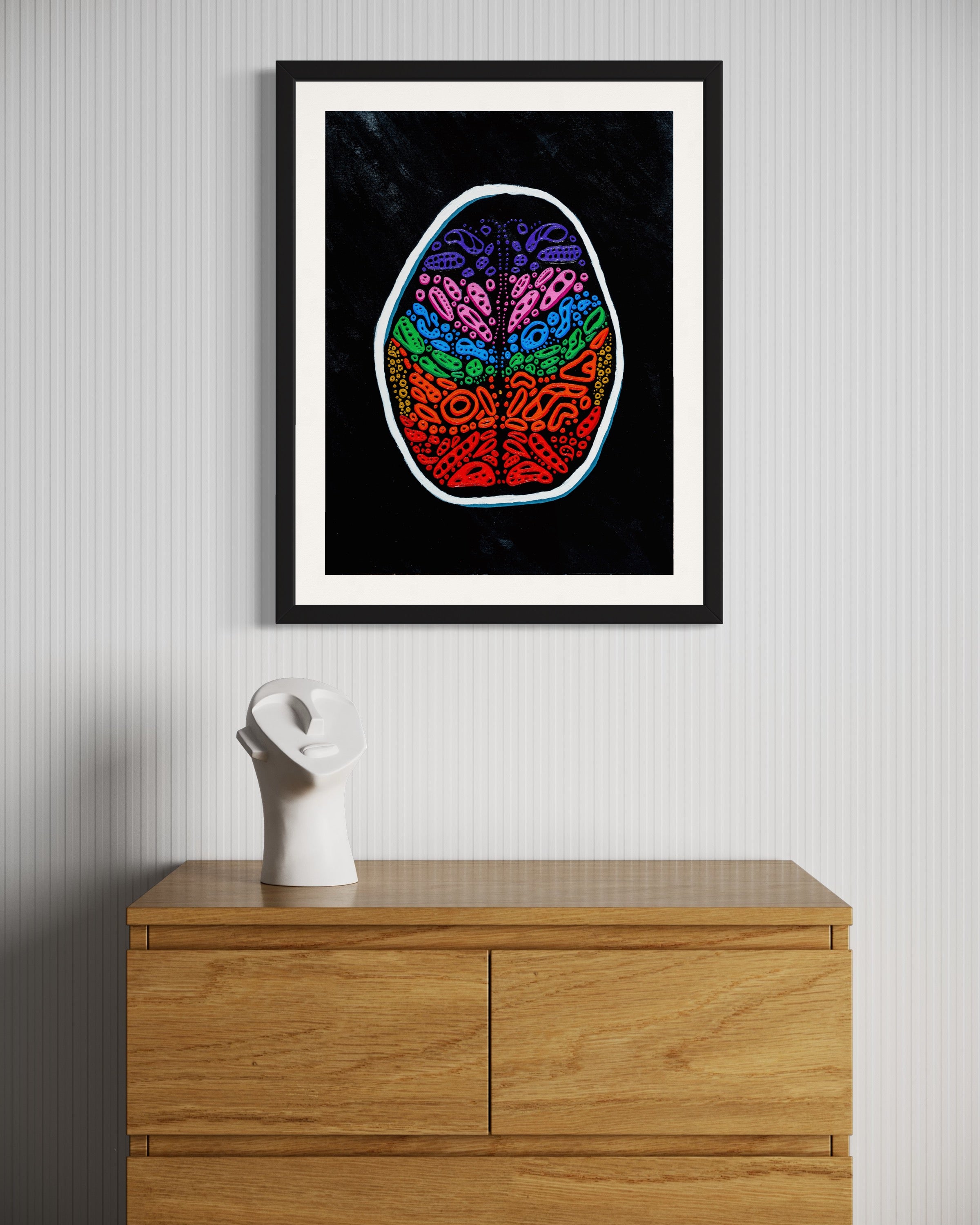 A framed artwork depicting a multicolored illustration of a human brain, displayed on a wall above a wooden cabinet. Front view of ‘Penumbra Painting No. 2’ by Nicholas Hayes. Original 18x24 inch acrylic on heavyweight canvas paper in a sleek black frame, contemporary abstract wall art, one-of-a-kind piece ready to hang.